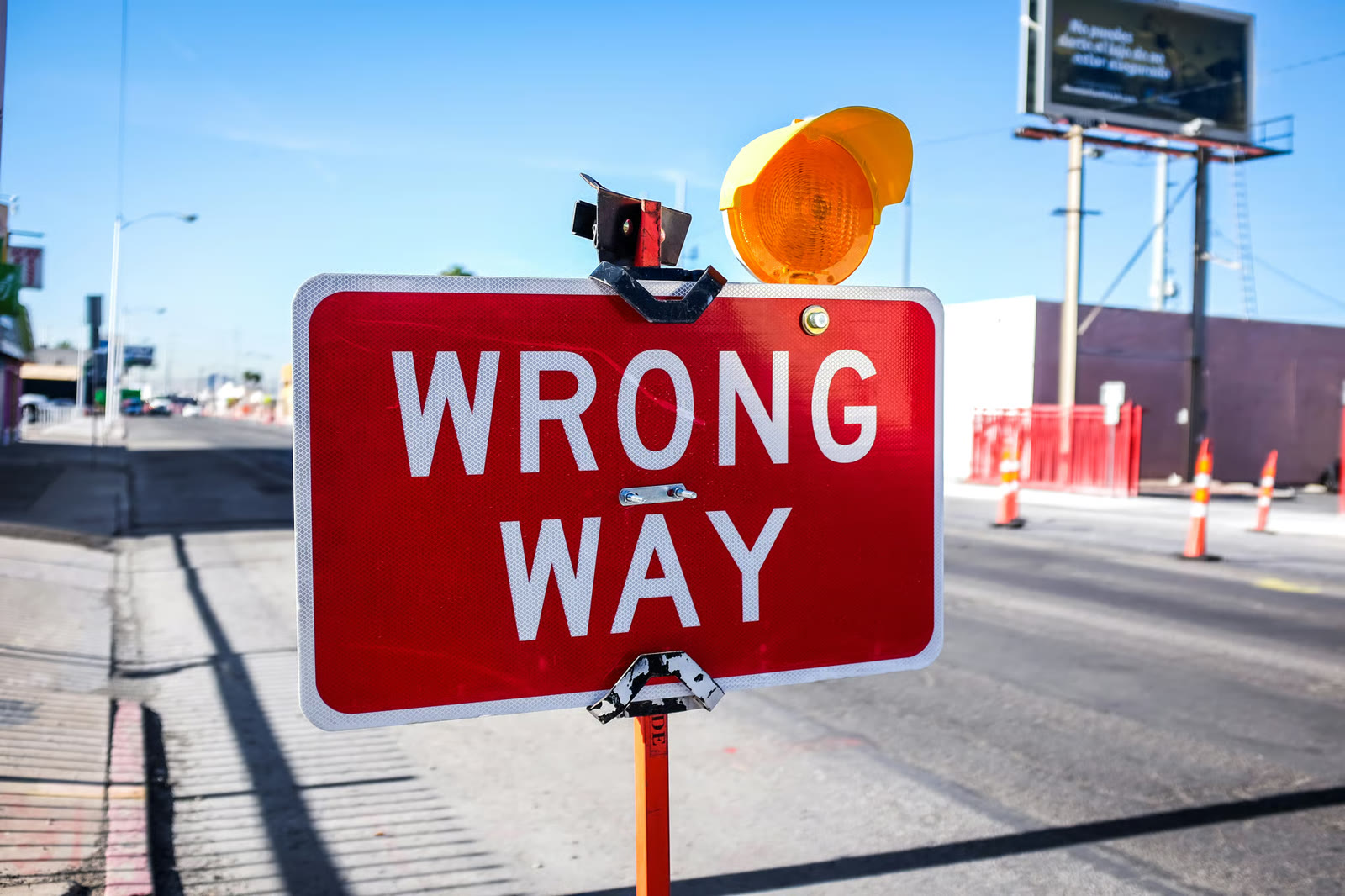 A red WRONG WAY traffic sign at a city intersection, topped with an amber warning light.